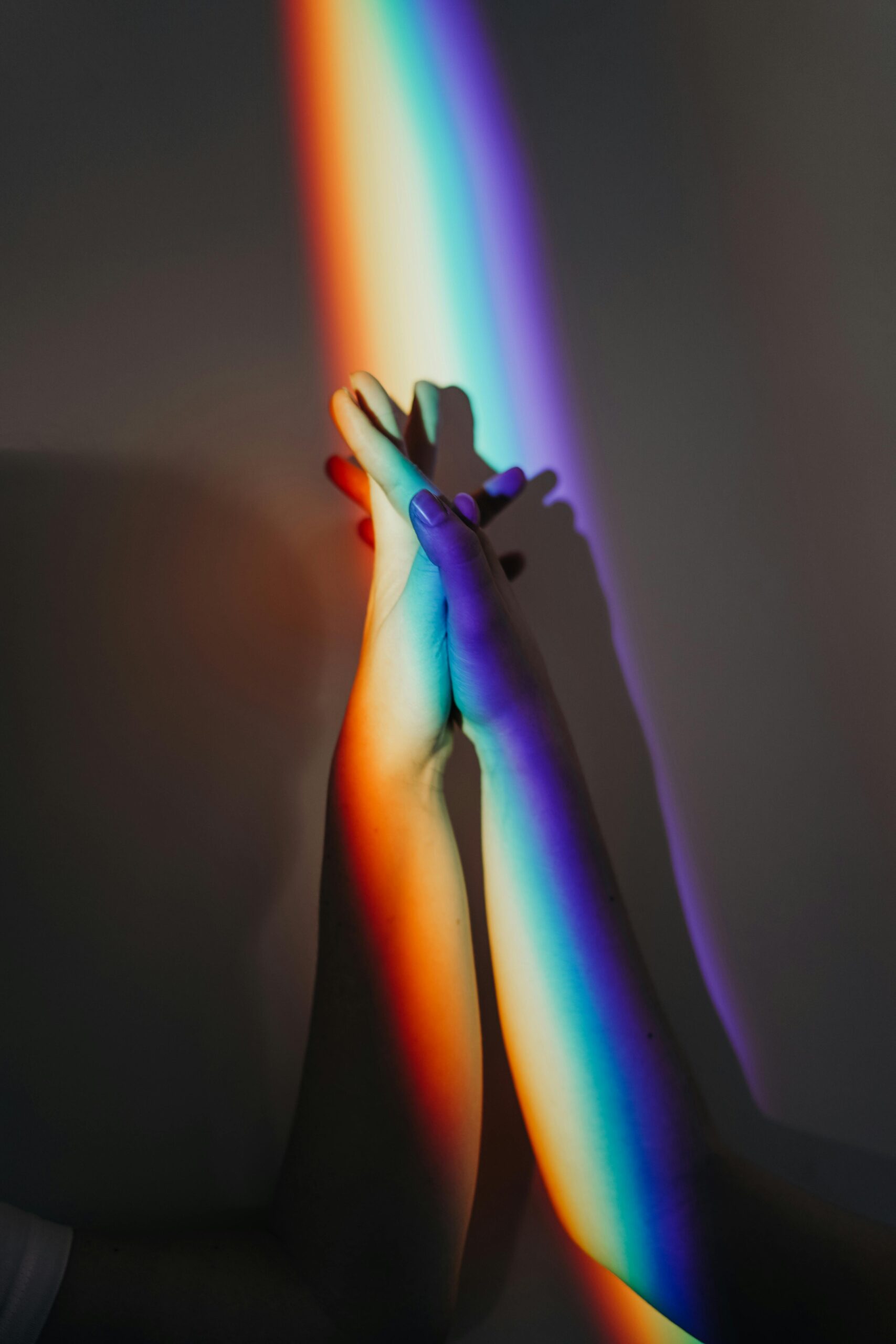 Two white hands are interlocked beneath a projected streak of rainbow