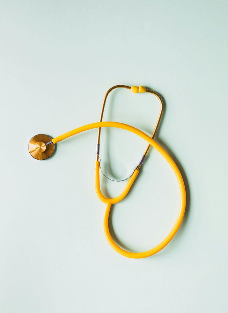 A yellow stethoscope lays on a pastel blue background